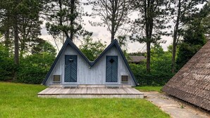 A small, rustic cabin with a steeply pitched roof and a symmetrical design, featuring two doors and a small porch area.