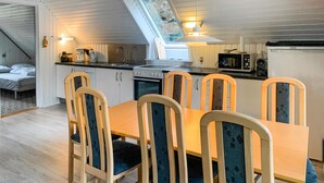 A compact kitchen with a dining area, featuring a wooden table and chairs, a microwave, a coffee maker, and a sink.