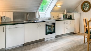 A compact kitchen with white cabinets, a stainless steel sink, a built-in oven, and a microwave. There's a skylight above the sink and a framed picture on the wall.