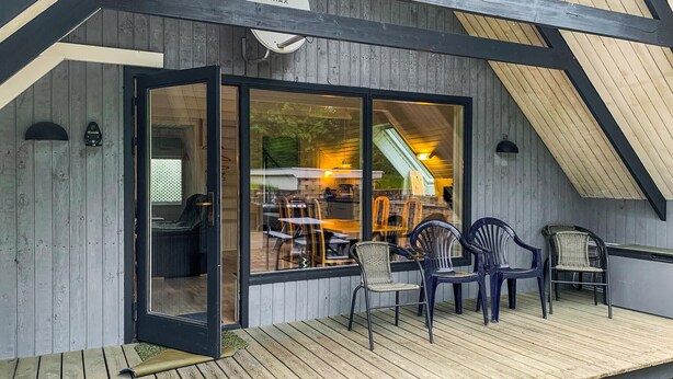 A wooden deck with outdoor seating and a glass door leading to an interior space with tables and chairs.
