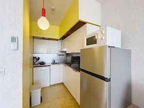 A compact kitchen with white cabinets, a stainless steel refrigerator, a microwave, and a hanging light fixture.