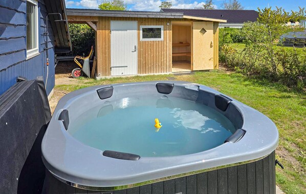 A hot tub in a backyard with a wooden deck, a shed, and a lawn.