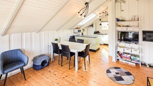A modern kitchen with white cabinets, a dining area with a white table and black chairs, a blue pet bed, and a wooden floor. - Lovely home in Grenaa with sauna (Grenaa)