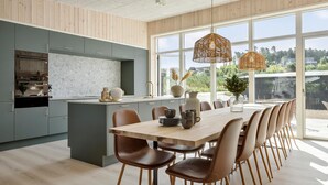 Une cuisine moderne avec des meubles gris, un pare-feu en marbre et un grand îlot central. On y trouve également un coin repas avec une table en bois et des chaises marron.