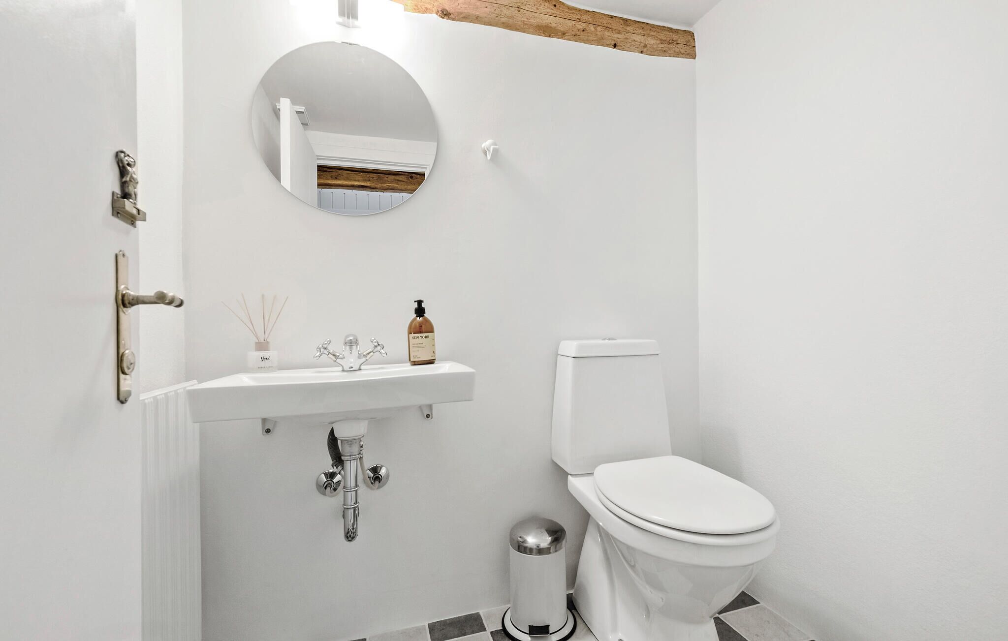 Un bany amb un lavabo blanc, un mirall, un vàter i un cub de la brut.
