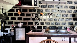 A kitchen with a microwave, stove, and sink. There is a brick-patterned backsplash and a wooden chair.