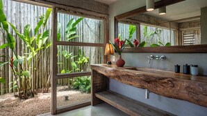 A bathroom with a wooden vanity, a mirror, and a view of a bamboo garden. - Your luxury home in the heart of Trancoso (Trancoso)