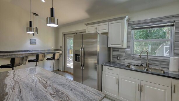 A modern kitchen with a marble countertop, stainless steel appliances, and pendant lighting.