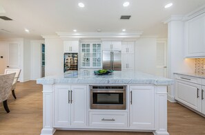 A modern kitchen with white cabinetry, a marble countertop, stainless steel appliances, and a built-in oven.
