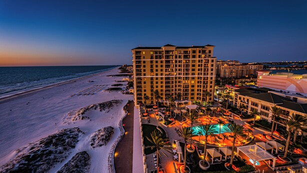 A beachfront hotel with multiple floors, a swimming pool, and a well-lit outdoor area.