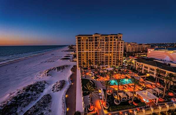 A beachfront hotel with multiple floors, a swimming pool, and a well-lit outdoor area.