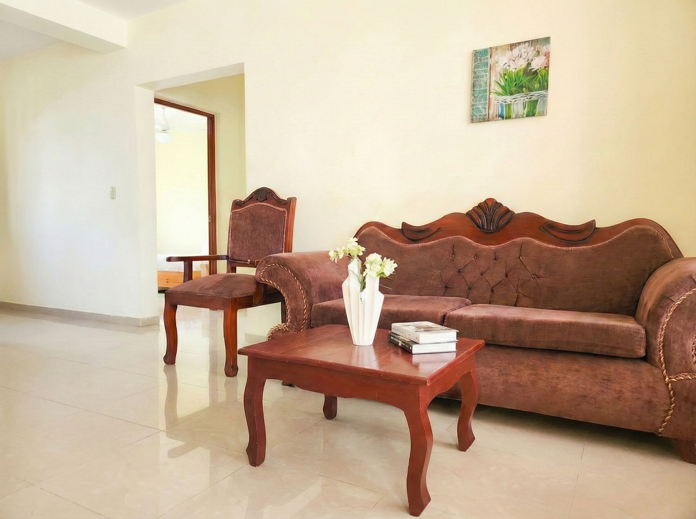 A living room with a brown sofa, a wooden coffee table, and a chair. There is a vase with flowers on the table.