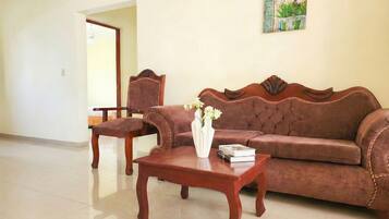 A living room with a brown sofa, a wooden coffee table, and a chair. There is a vase with flowers on the table.