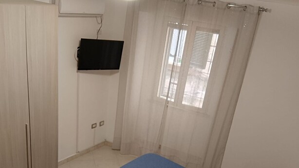 Un dormitorio con cama, televisión en la pared y ventana con cortinas.