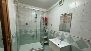 Un baño con ducha de vidrio, un lavamanos blanco y un espejo encima.