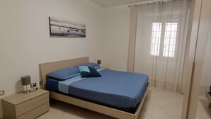 Un dormitorio con cama, mesita de noche, lámpara y ventana con cortinas.