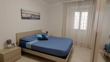 Una camera da letto con un letto, un comodino, una lampada e una finestra con tende.