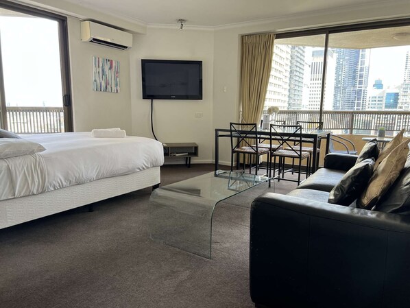 Ein Hotelzimmer mit Bett, Fernseher, einem Balkon mit Tisch und Stühlen sowie Blick auf die Stadt.