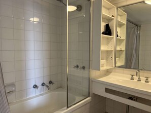 Ein modernes Badezimmer mit einer gläsernen Dusche, einem weißen Waschbecken mit Spiegel und einem gefliesten Boden.