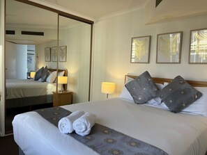 Ein Hotelzimmer mit einem großen Bett, zwei Nachttischen, einem Spiegel und drei gerahmten Kunstwerken an der Wand.