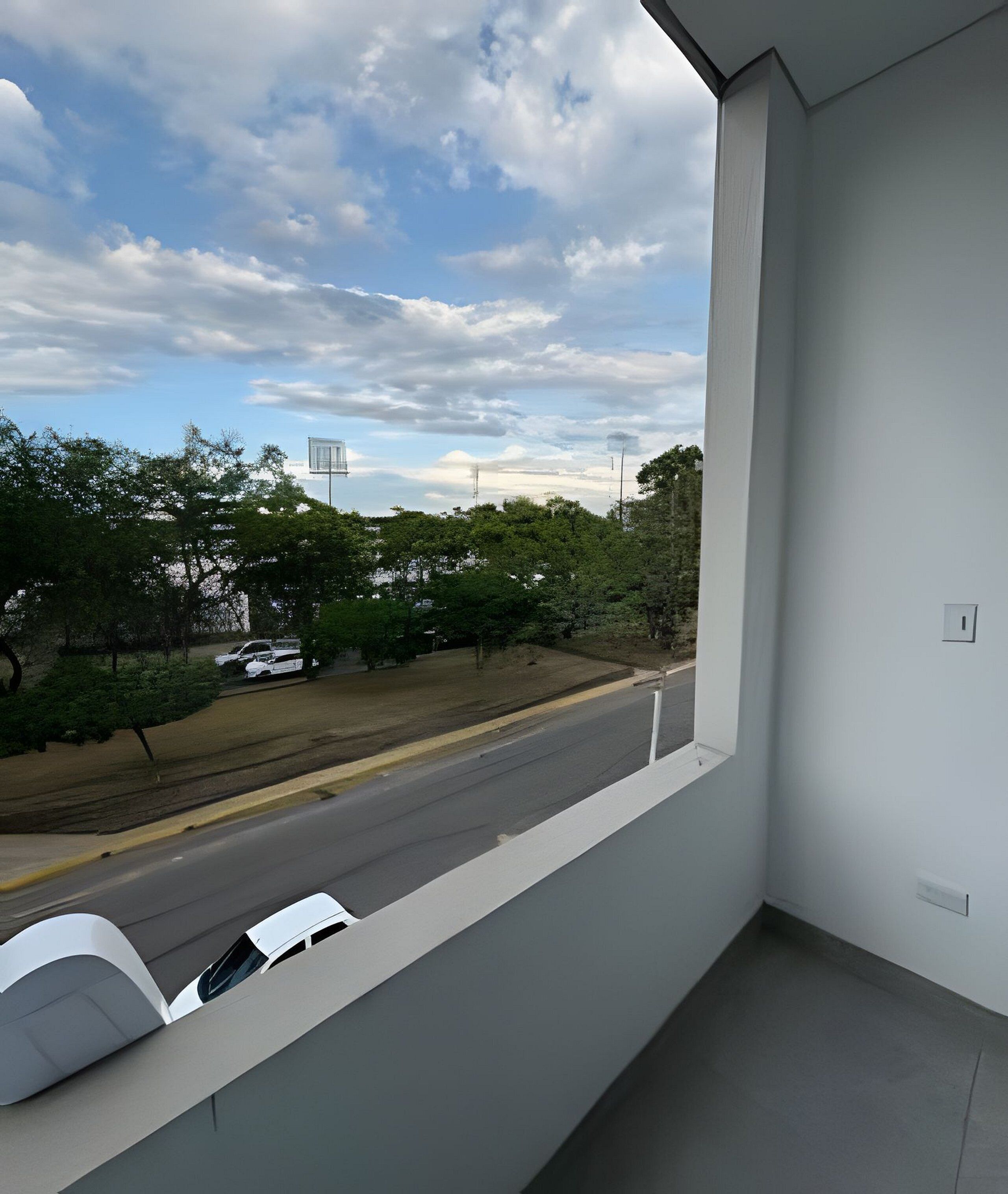 Un balcon donnant sur une route, des arbres et un ciel nuageux.