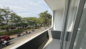 Un balcon donnant sur une rue, un immeuble et des arbres.
