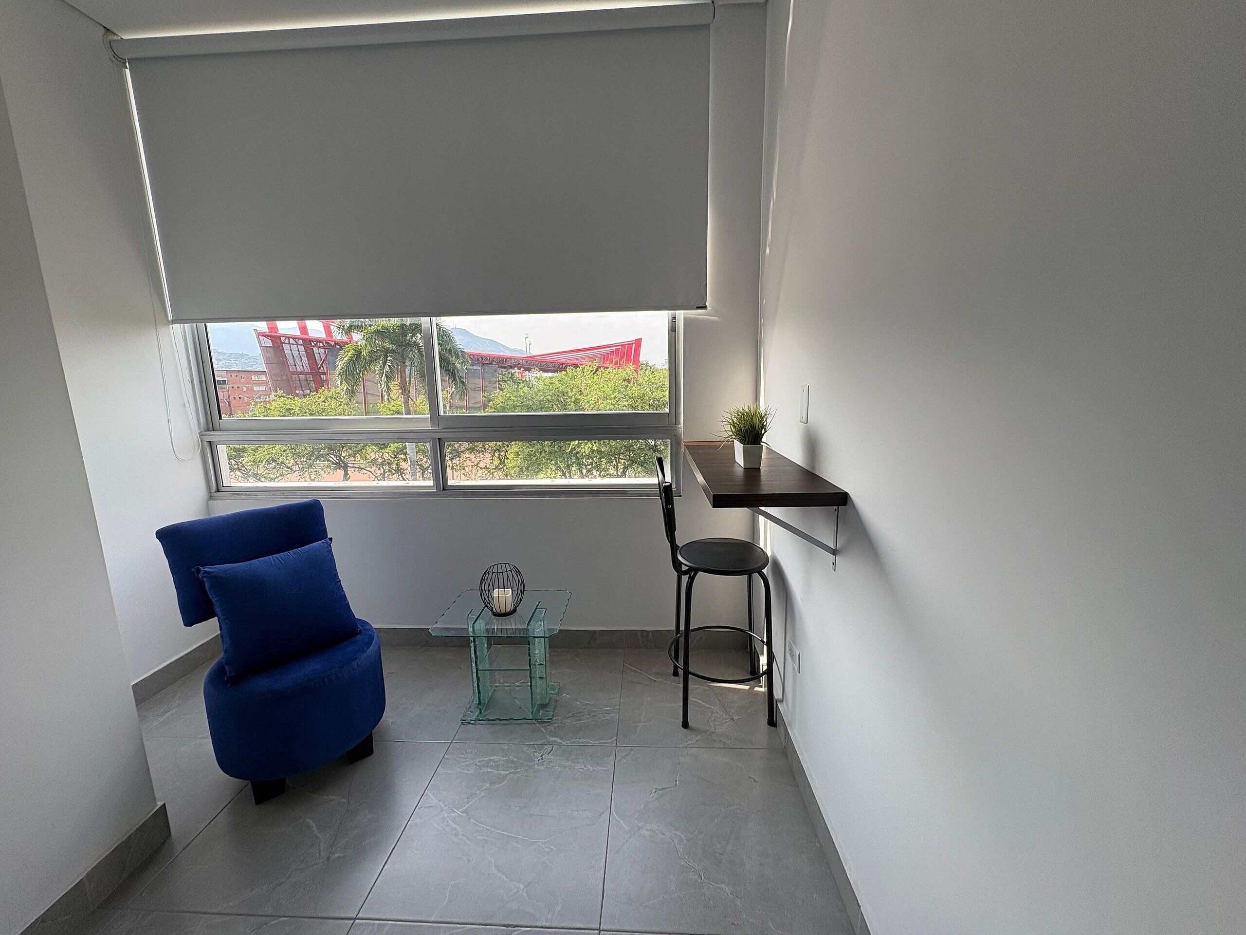 A small room with a blue chair, a glass table with a candle, and a plant on a shelf.