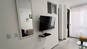 Un salon moderne avec un téléviseur fixé au mur, un grand miroir et une petite fenêtre.