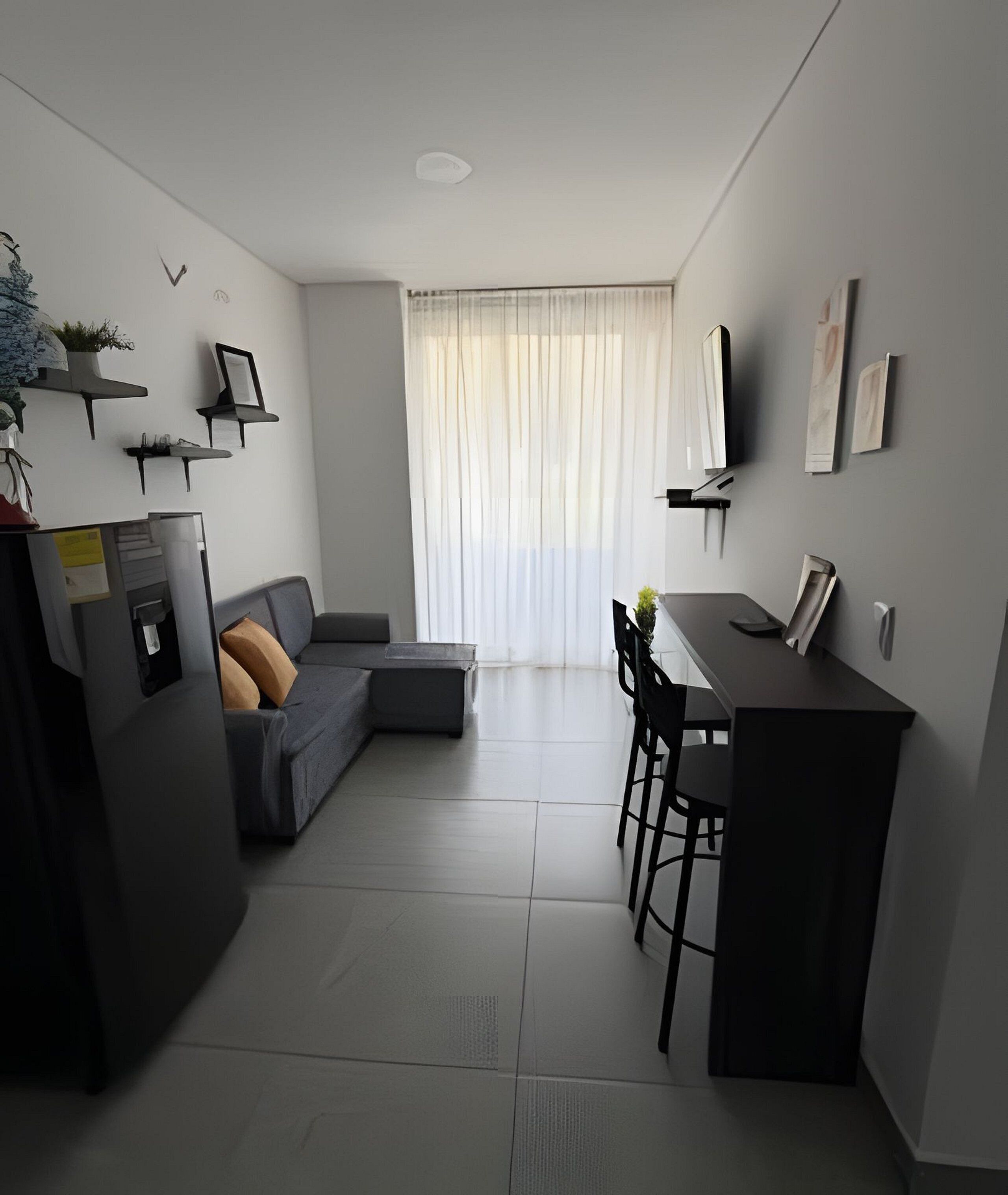 A modern kitchen with a dining area, a sofa, and a TV mounted on the wall.