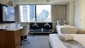 A hotel room with a desk, a sofa, a bed, and a large window with a city view.