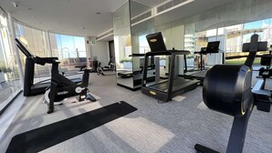 A modern gym with cardio machines, a mirrored wall, and large windows offering a city view. - Large City Studio with Big Balcony (Darlinghurst)