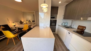 A modern kitchen with a central island, white cabinetry, and a microwave. - Large City Studio with Big Balcony (Darlinghurst)