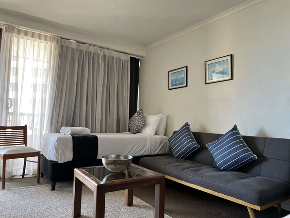 A hotel room with a bed, a sofa, a chair, a coffee table, and two framed pictures on the wall.