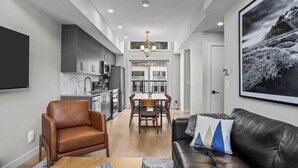 A modern living room with a black leather sofa, a brown leather armchair, and a dining area with a table and chairs.