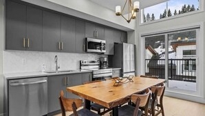 A modern kitchen with grey cabinets, stainless steel appliances, and a wooden dining table with four chairs.