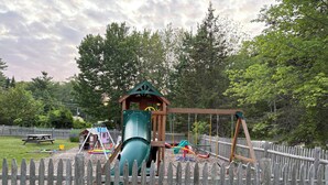A playground with a slide, swings, and a small playhouse.