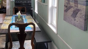 A dining area with a table set for two, a clock on the wall, and a beach-themed painting on the wall.