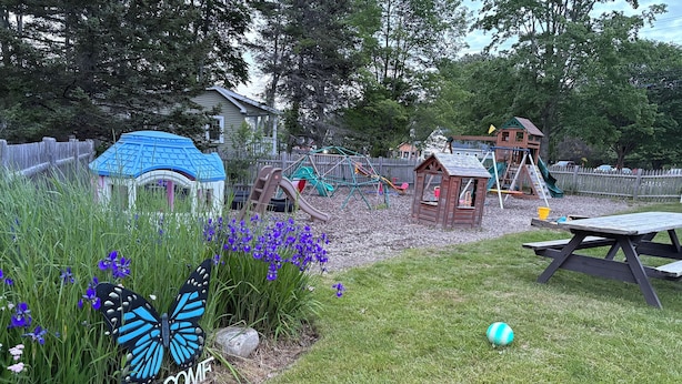 A backyard with a play area, a picnic table, and a welcome sign with a butterfly decoration.