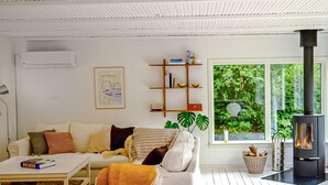 A modern living room with a white sofa, a coffee table, a bookshelf, a fireplace, and a window with a view of greenery.
