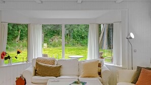 A room with a white sofa, a coffee table, and a view of a garden through large windows.