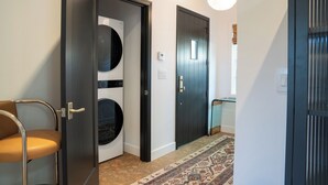 A hallway with a modern design, featuring a black door, a white door, and a beige chair. - Spanish-style garden bungalow! (Burbank)