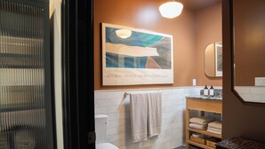 A modern bathroom with a toilet, sink, and a framed abstract painting. - Spanish-style garden bungalow! (Burbank)
