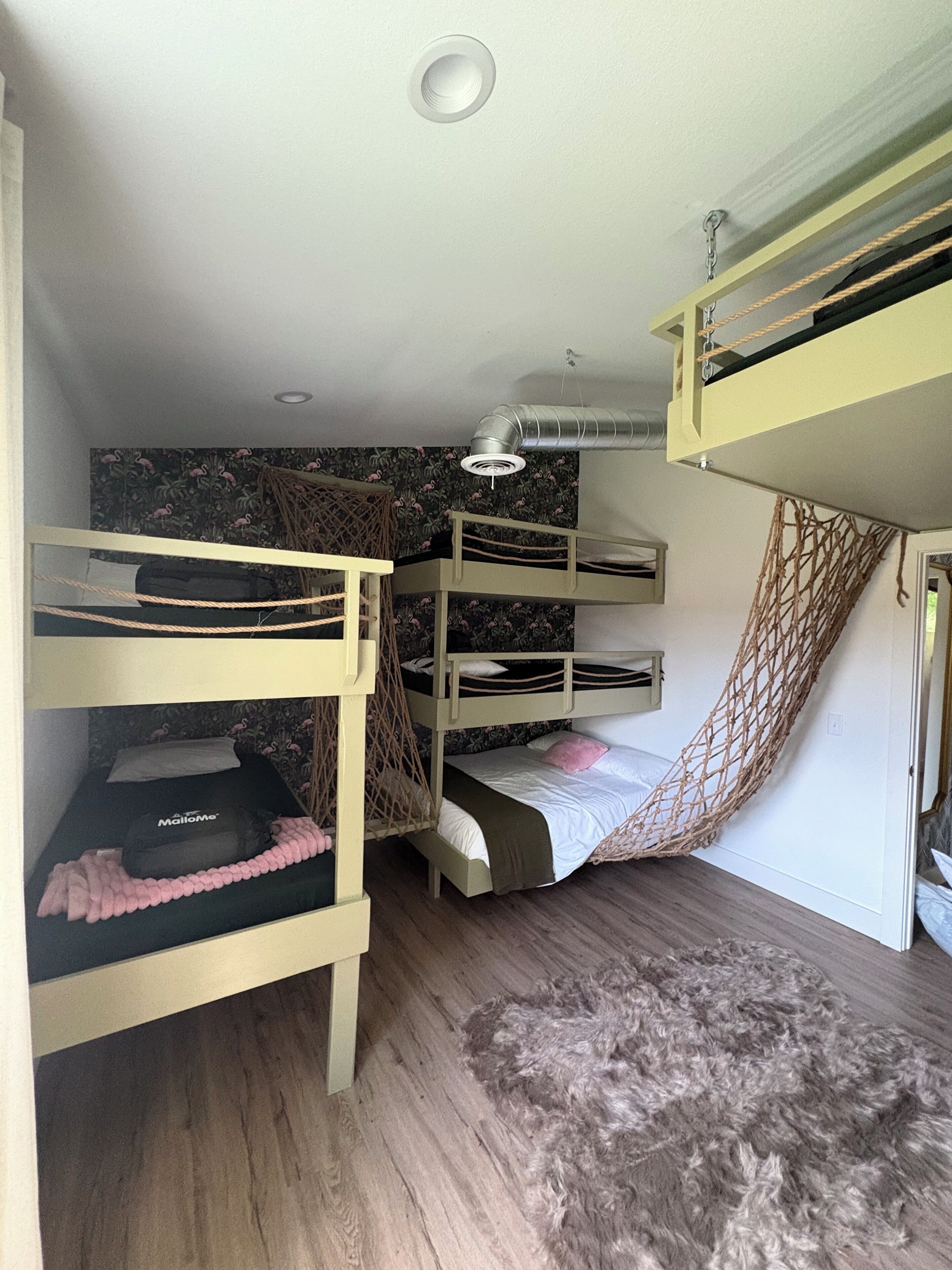Une chambre avec un lit superposé, un hamac, un petit bureau et un tapis.