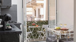 Una cocina con estufa a gas, un comedor con mesa puesta para dos personas y un balcón con mesa y sillas.