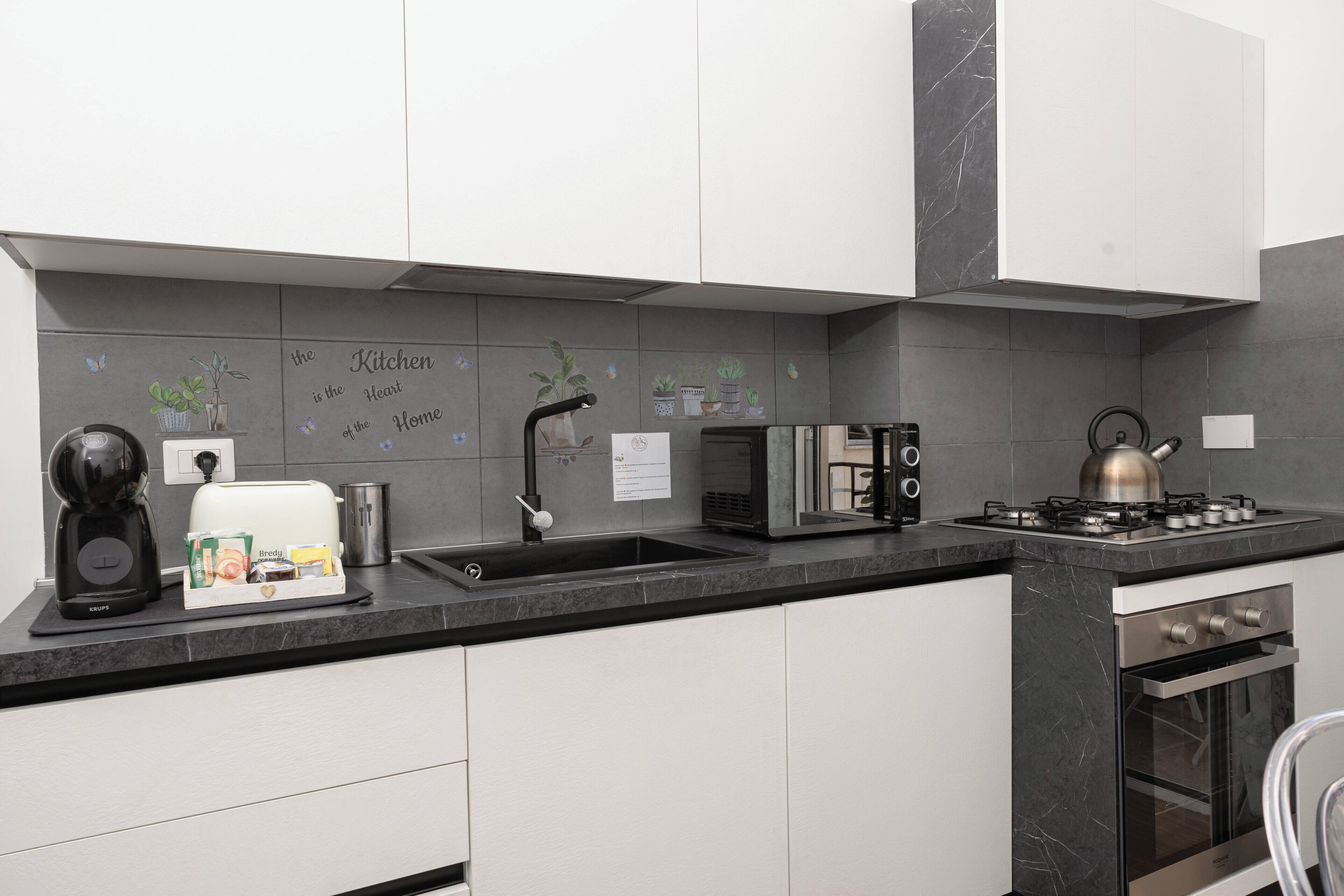 A modern kitchen with white cabinets, a black countertop, a kettle, a toaster, and a sink.