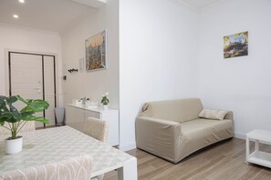 Ein modernes Wohnzimmer mit einer Couch, einem Esstisch mit Pflanze und einer Küchenzeile mit Arbeitsplatte und Schränken.