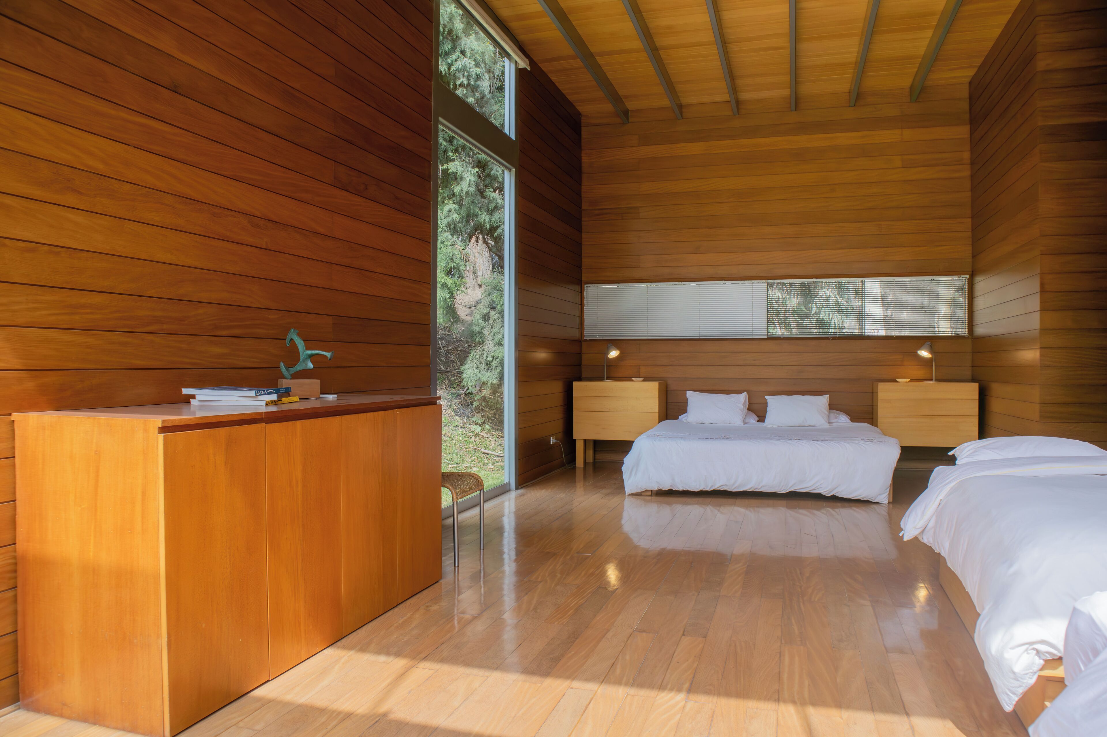 Une chambre moderne avec un lambris en bois, un bureau, deux lits et une grande fenêtre offrant une vue sur l’extérieur.