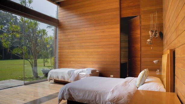 A modern bedroom with two beds, wooden walls, a large window, and a view of greenery. - Casa Cieneguilla by Wynwood House (Pachacamac)