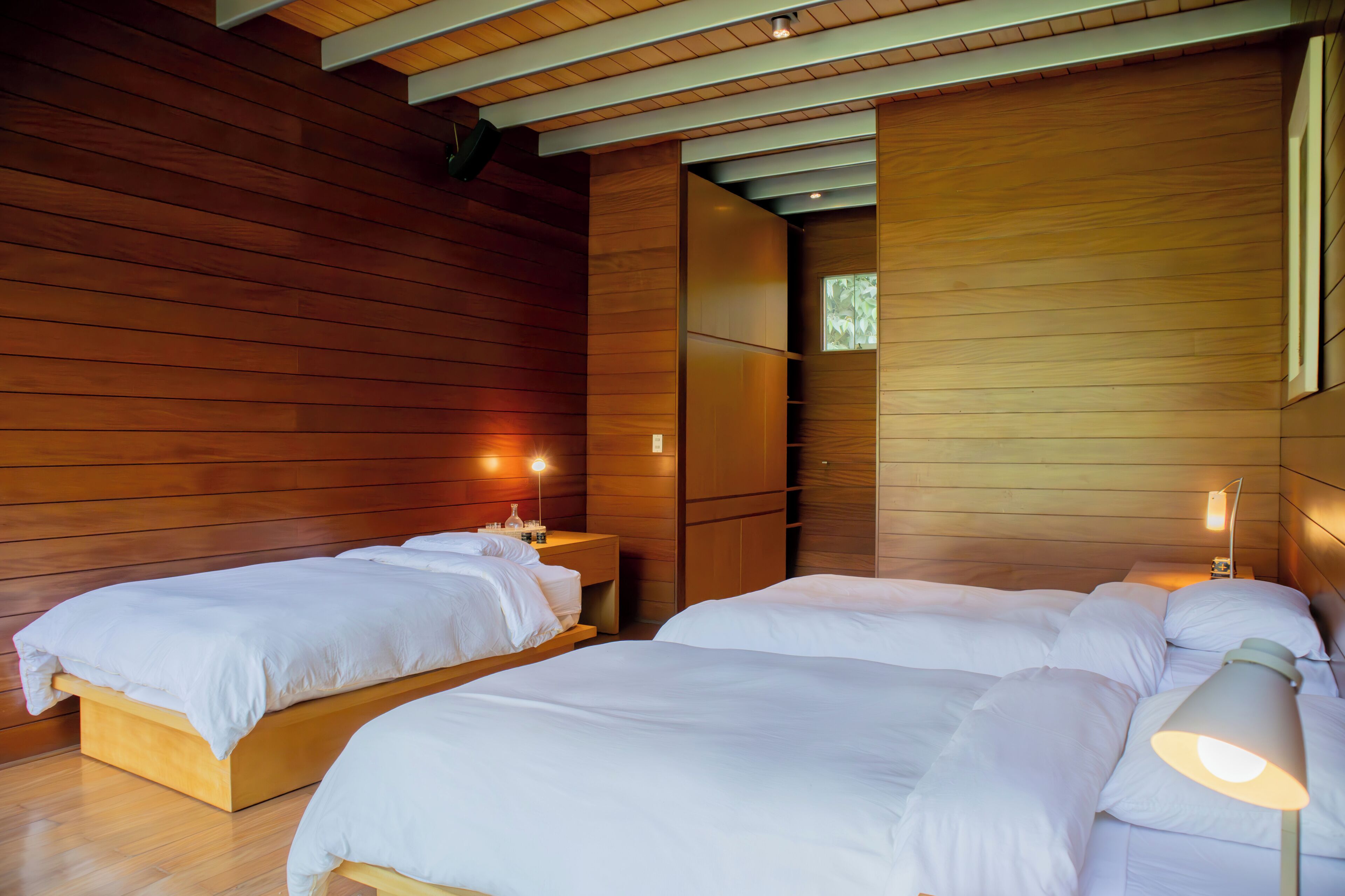 Una habitación con dos camas, paredes de madera y un ventanal pequeño.