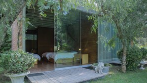 A modern glass-enclosed bedroom with a wooden deck, a bed, and a bedside table. - Casa Cieneguilla by Wynwood House (Pachacamac)